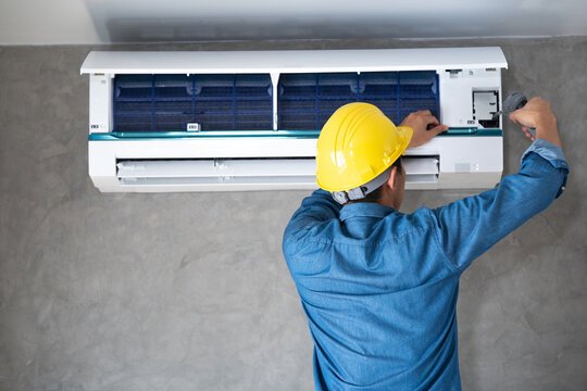 a man wearing a hard hat and working on a air conditioner